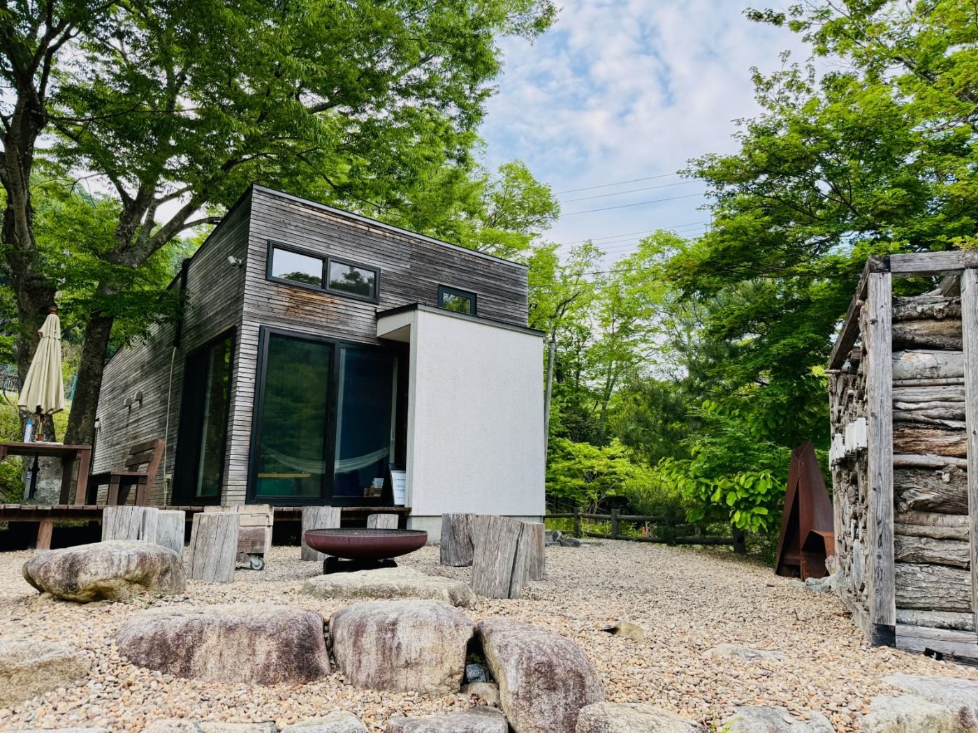 黒い木サウナ小屋の外観と野外の焚火台